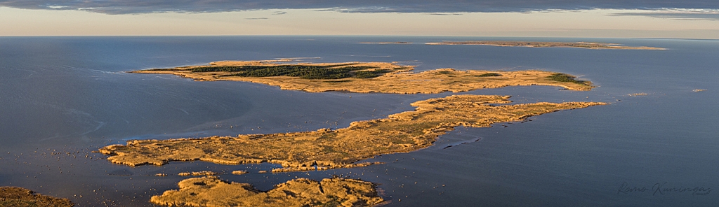 Panoraam aerofoto Kasti hoiualas olevatest saartest kuldse hommikupäikese valguses. Taamal on näha ka Abruka saart horisondi all. (Saaremaa)